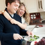 05-engaged-couple-kitchen-man-cutting-vegetables-woman-hugging-smiles-grapes-cuff-bracelet-ring