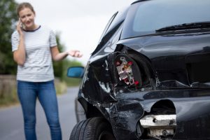 Unhappy Female Driver With Damaged Car After Accident Calling Insurance Company On Mobile Phone