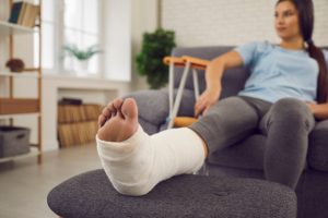 Female patient with broken leg in plaster cast sitting on sofa.